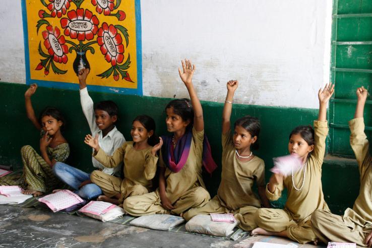 students sitting on floor in classroom with hands raised in air