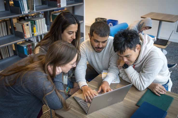 Four DEDP master's students looking at a laptop computer on MIT's campus. at laptop computer in t