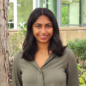 Headshot of an Indian woman with wavy black hair and an olive green shirt.