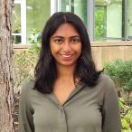 Headshot of an Indian woman with wavy black hair and an olive green shirt.